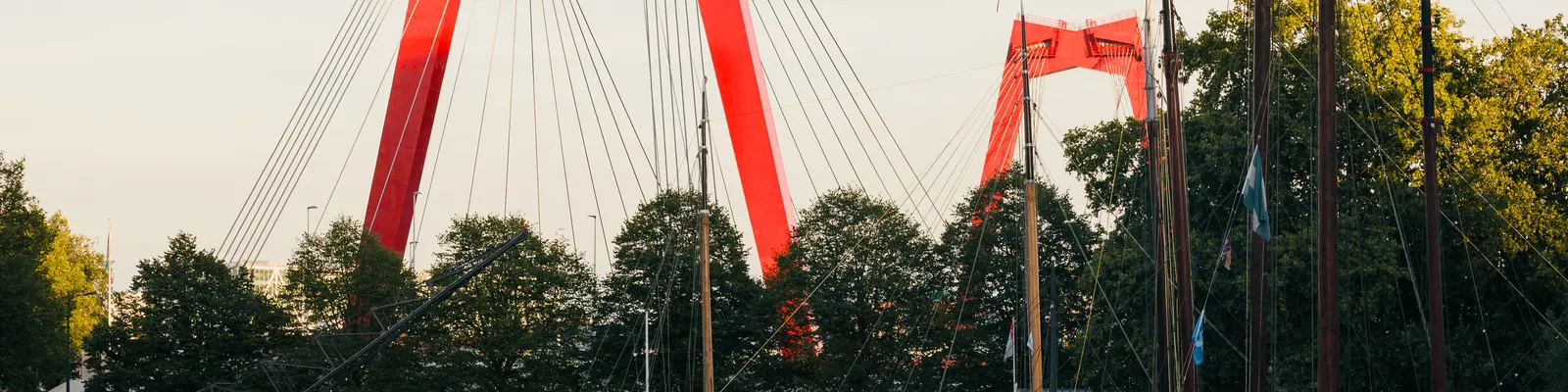 De rode Willemsbrug boven de Oude Haven in Rotterdam, met masten van aangemeerde schepen ervoor.